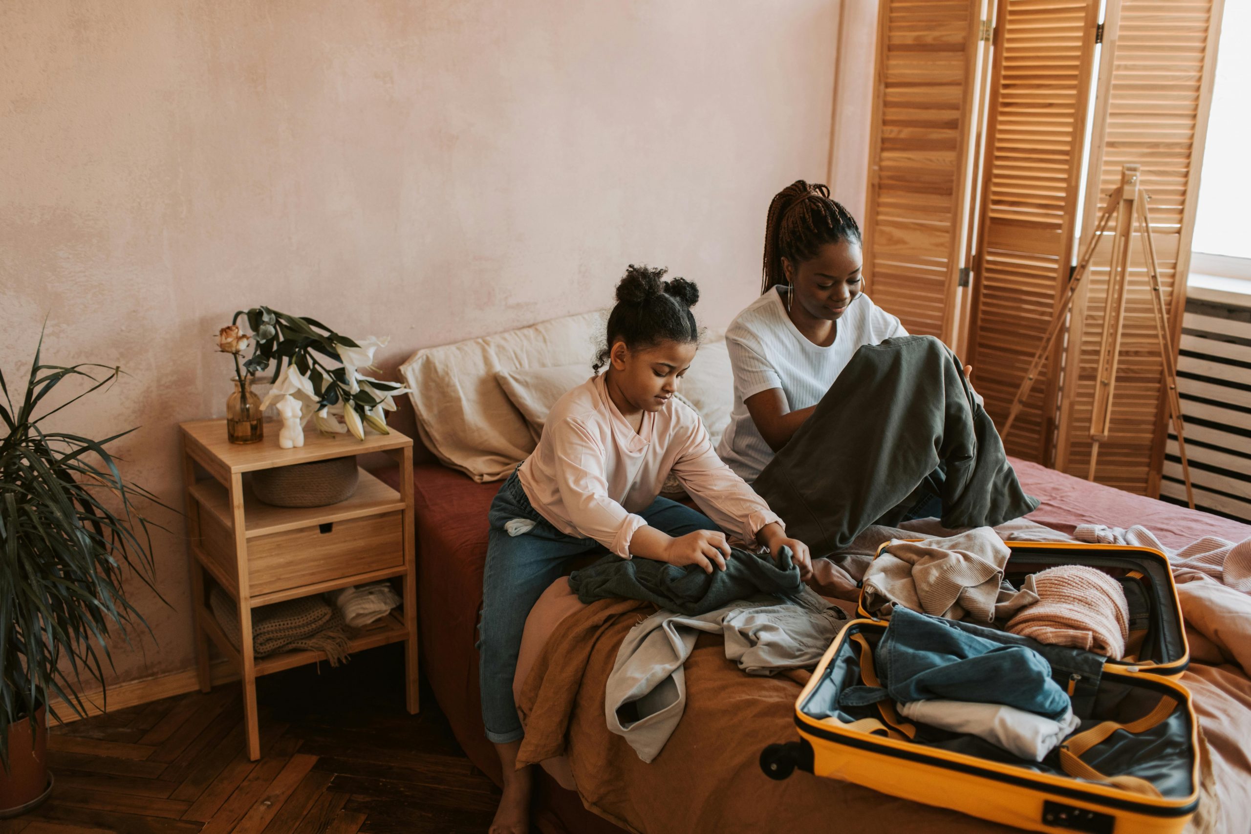 mother and daughter packing clothes into a suitcase in a bedroom