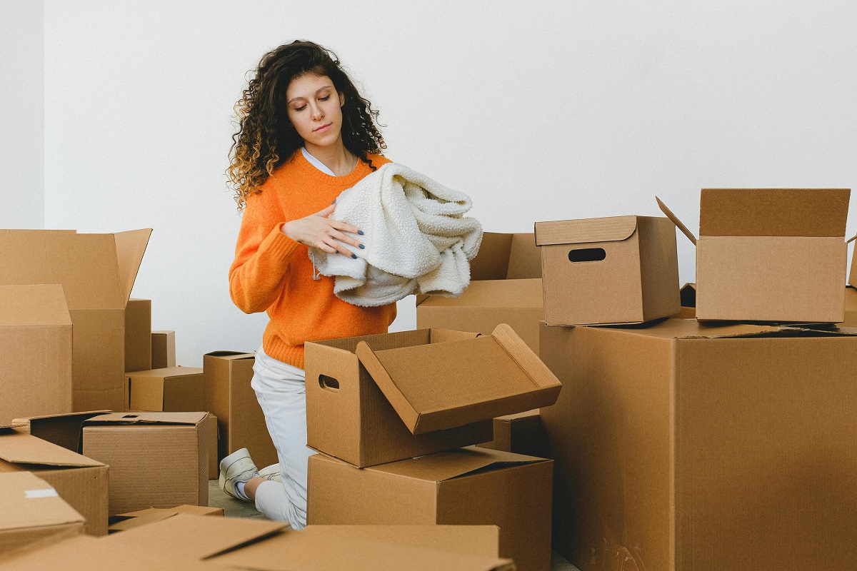 woman in an orange sweater packing a wool jacket into a moving box