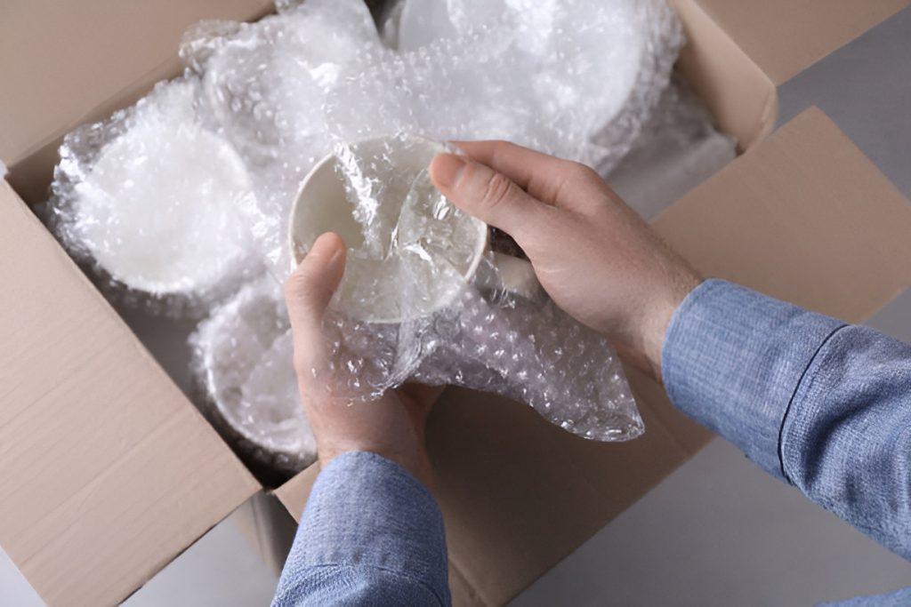 person wrapping bowls using bubble wrap and putting them in a moving box